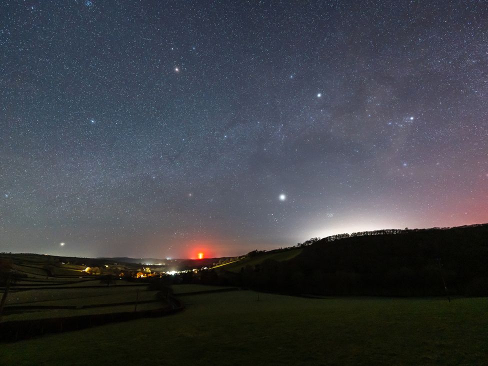 A night sky filled with stars over hills and a town at Ceunant in Llanfihangel-y-Creuddyn near Aberystwyth