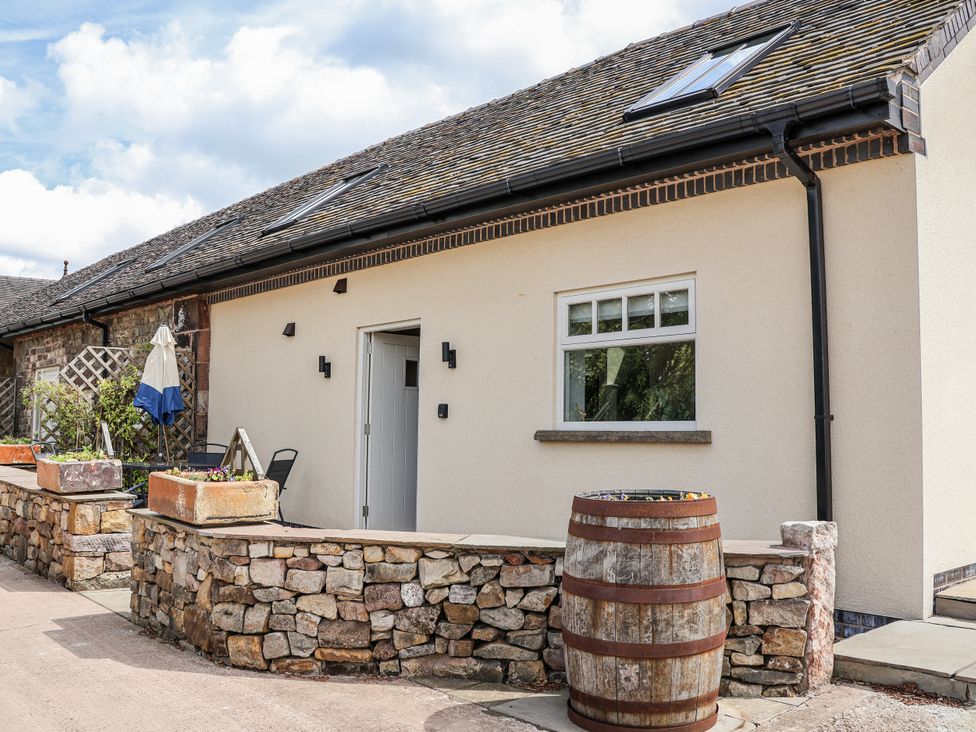 An outdoor area with a house, barrel, and planters at Fern Cottage in Biddulph