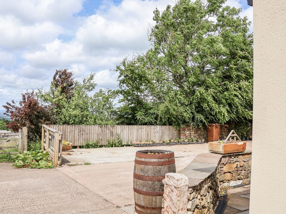 An outdoor space with trees, a fence, a barrel and a stone wall at Fern Cottage in Biddulph