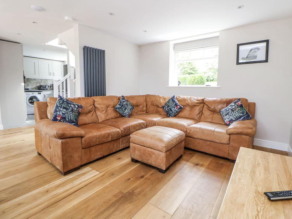 A living room with a brown sofa and footstool at Fern Cottage in Biddulph