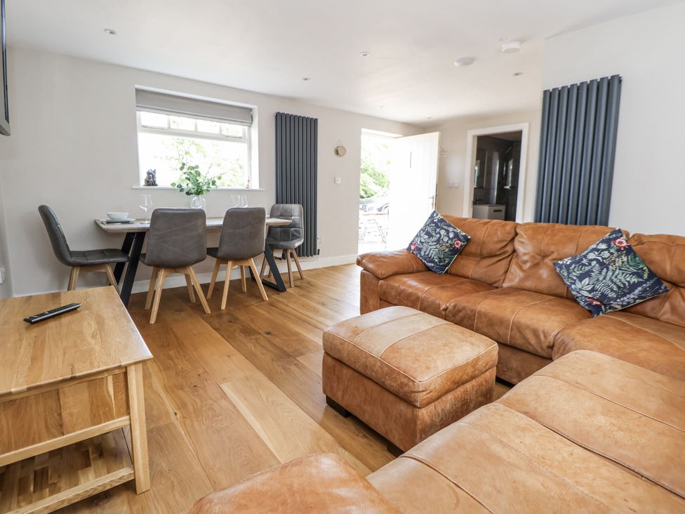 A living room with a brown leather sofa and dining area at Fern Cottage Biddulph
