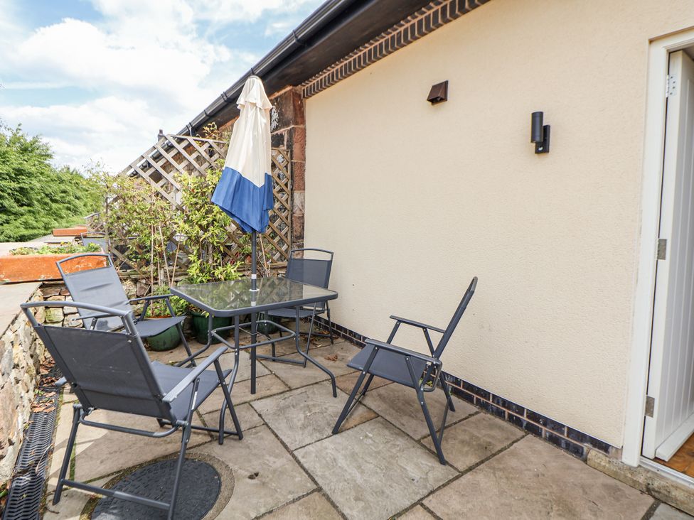 An outdoor patio area with a table, chairs, and an umbrella at Fern Cottage in Biddulph