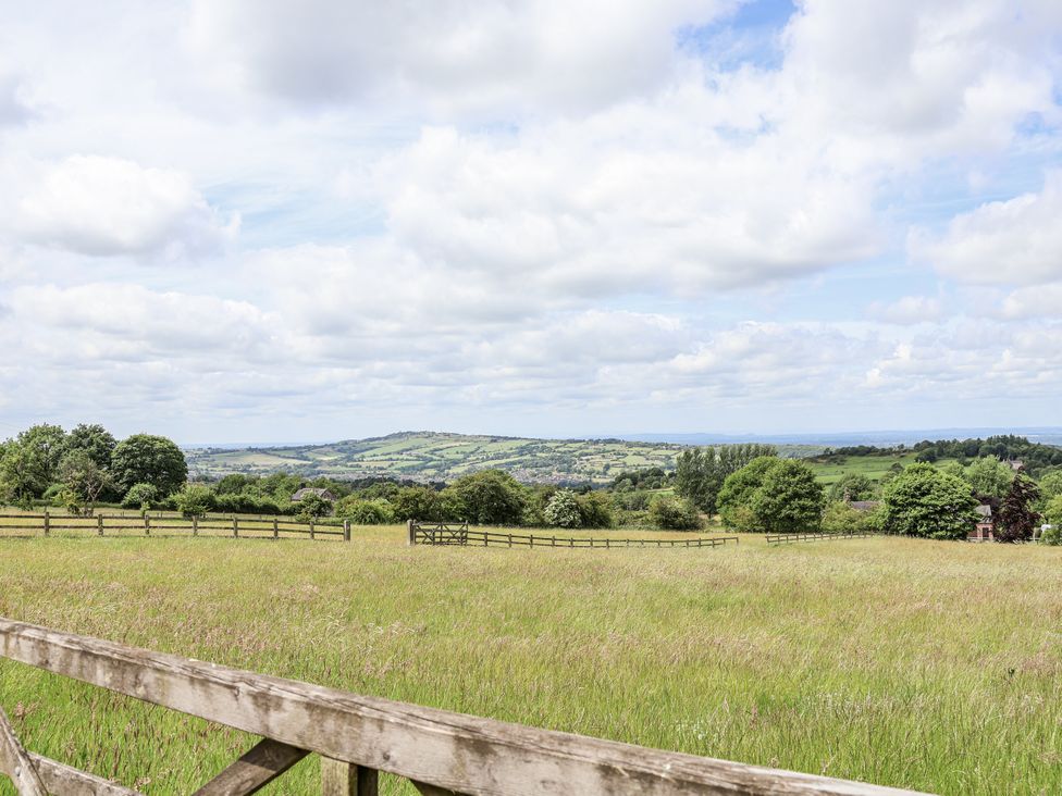 A field with a wooden fence and trees in the background at Fern Cottage in Biddulph