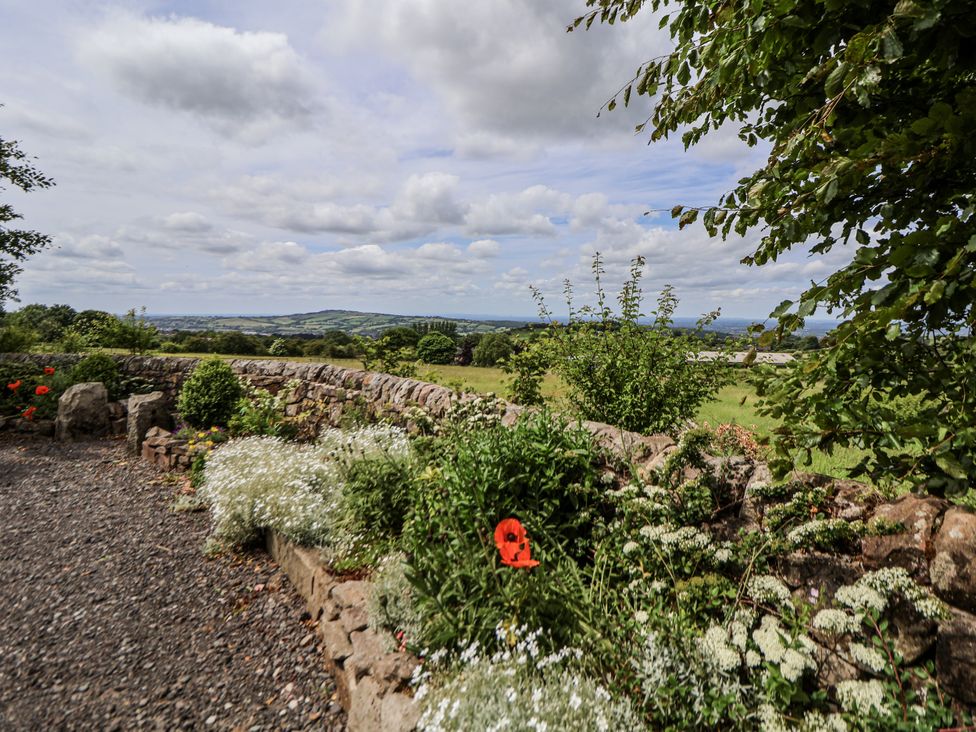 A garden with flowers and a stone wall overlooking a landscape at Fern Cottage in Biddulph
