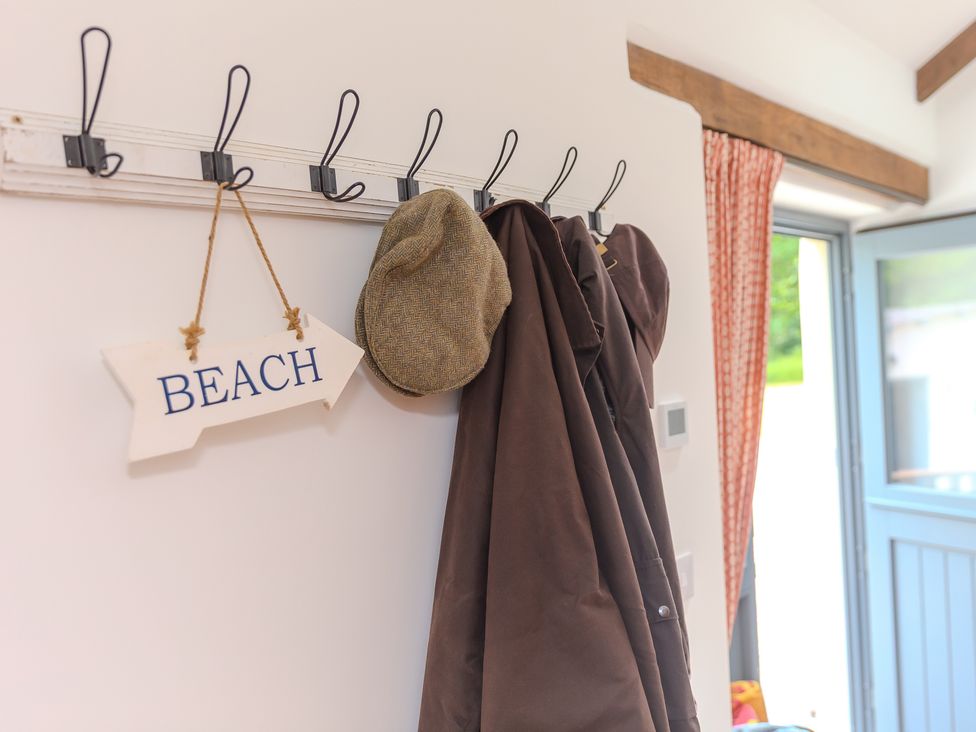 An entrance with a coat rack, a hat, and a beach sign at Carines Barns - Tre, Cubert