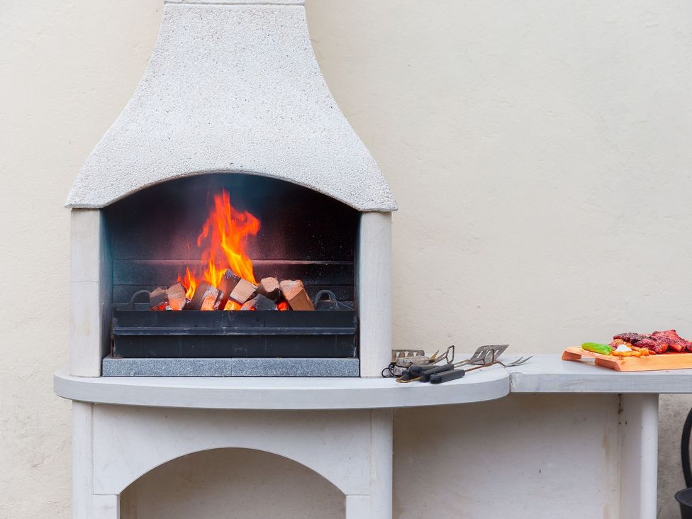 A fireplace with logs burning next to a cutting board at Carines Barns - Pol in Cubert