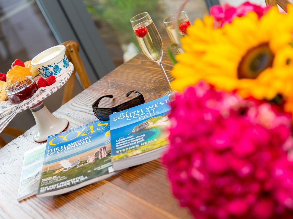 A table with magazines, glasses, scones, jam, strawberries, and flowers at Carines Barns - Wesley Barn in Cubert