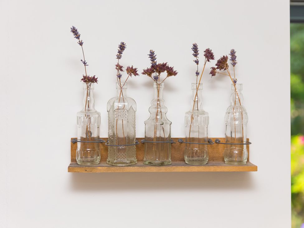 A wooden shelf holding glass bottles with dried flowers at Carines Barns - Wesley Barn, Cubert