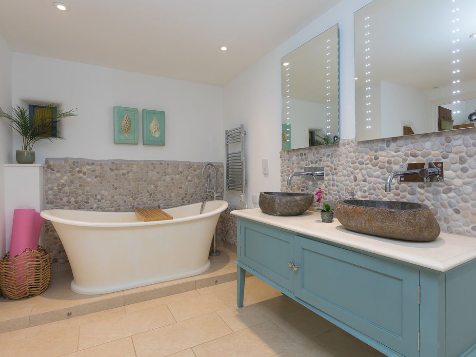 A bathroom with a bathtub and dual stone sinks at Carines Barns - Wesley Barn, Cubert