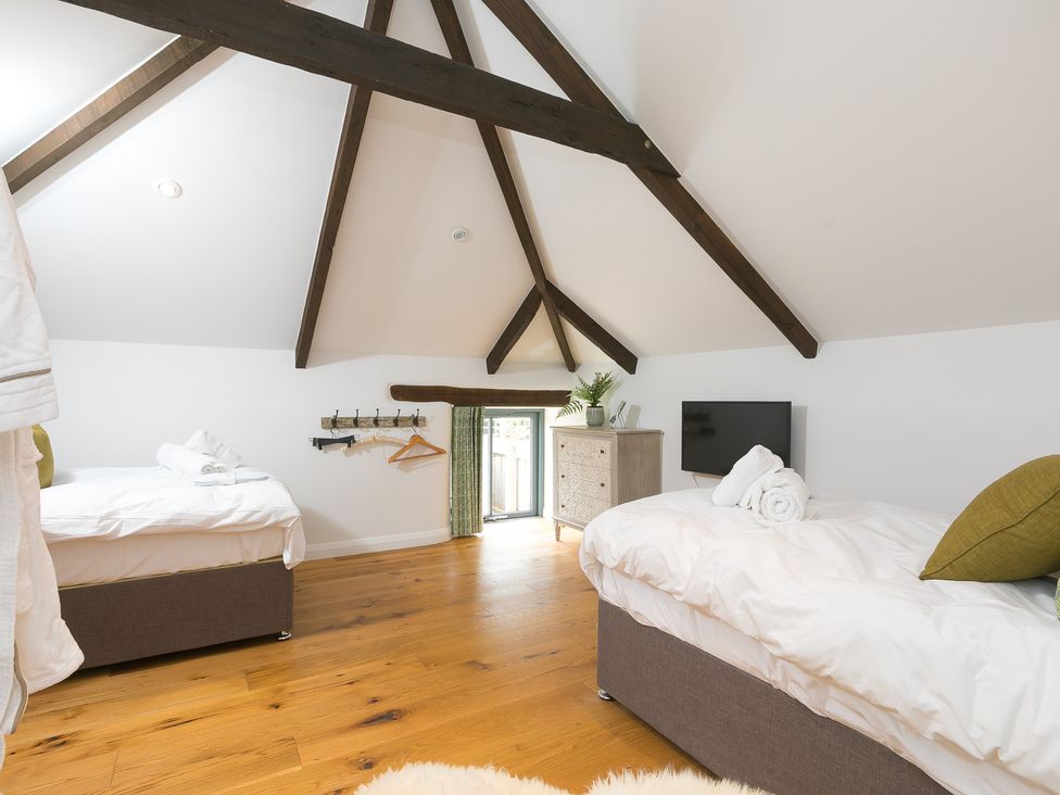 A bedroom with two beds and a television at Carines Barns - Wesley Barn, Cubert