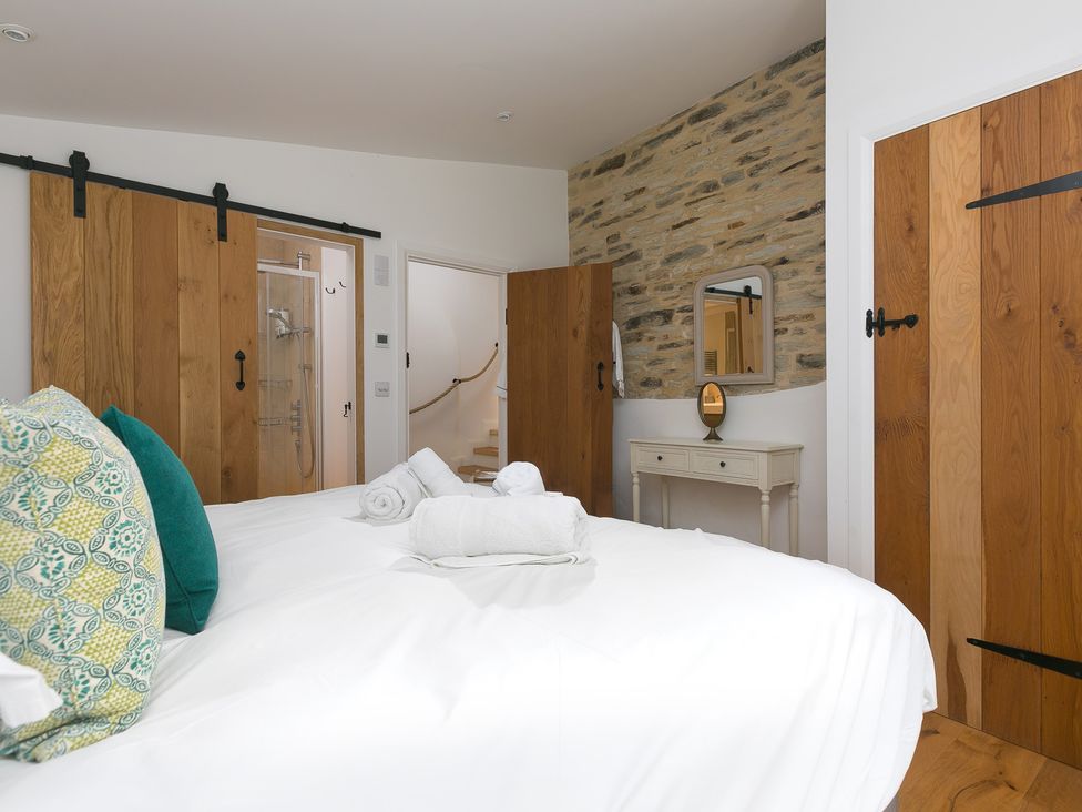 A bedroom with a bed and wooden doors at Carines Barns - Wesley Barn in Cubert