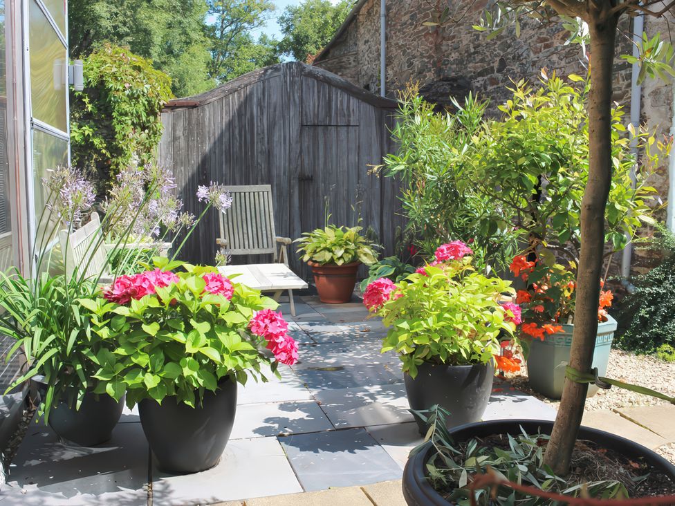A garden with flower pots and a chair at Barberry Brook in Dittisham