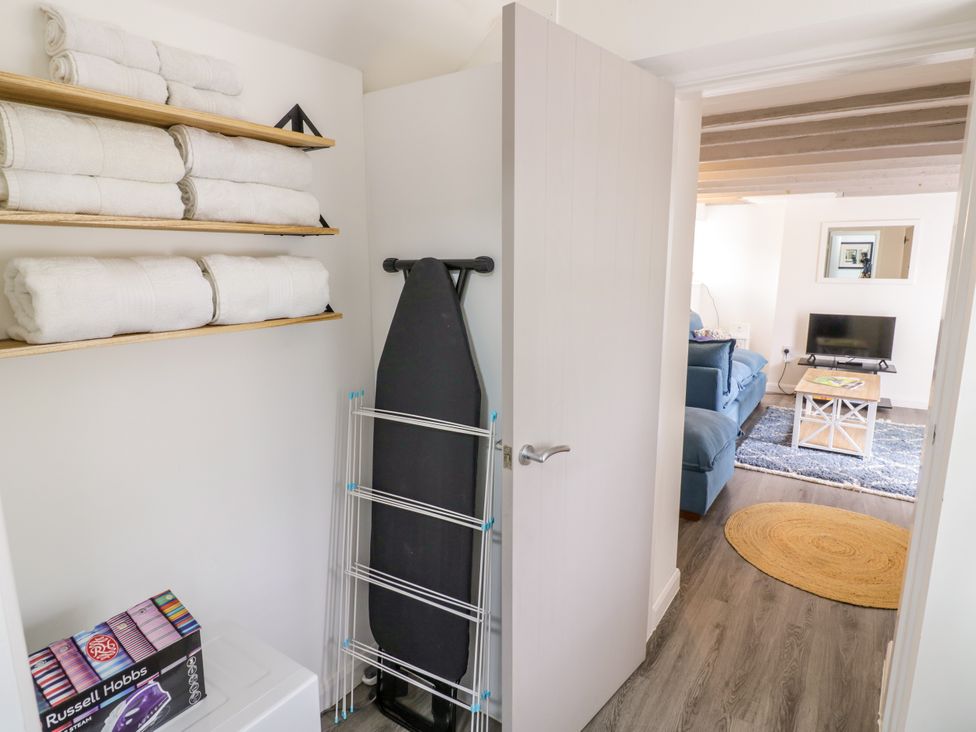 A utility room with towels and an iron board leading to a living area at The Cottage in Ettington
