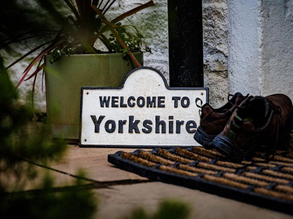 A welcome sign and shoes on a doormat at Wells Cottage in Holmfirth