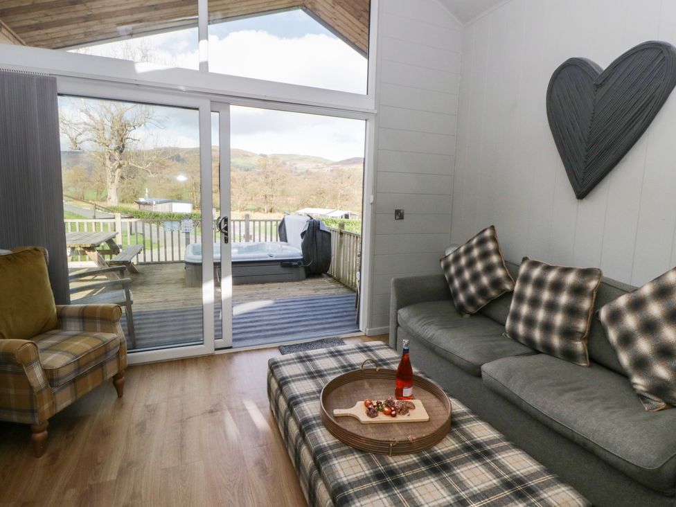 A living room with a sofa and armchair leading to a deck at Doe Lodge in Nantmel near Rhayader