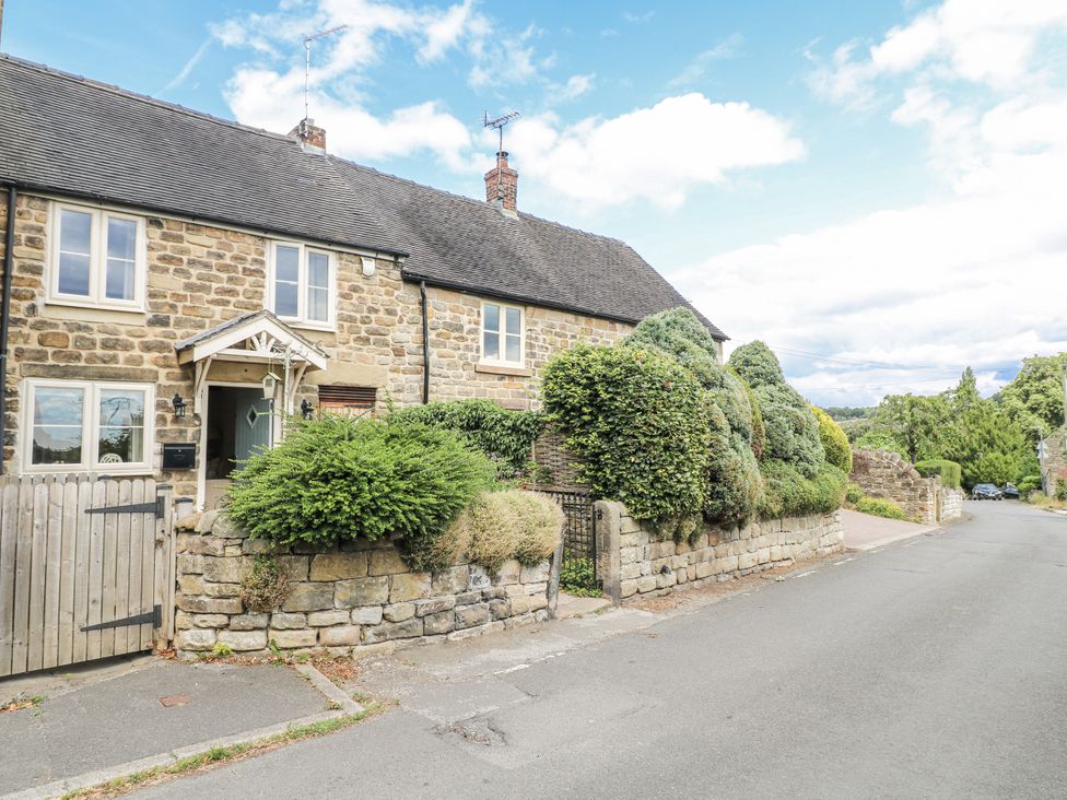 A stone house with a gated entrance and bushes at Clematis Cottage in Fritchley near Crich