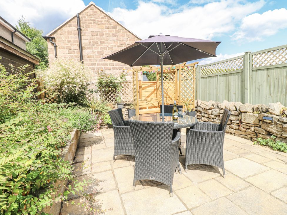 A garden with a table and chairs under an umbrella at Clematis Cottage in Fritchley near Crich