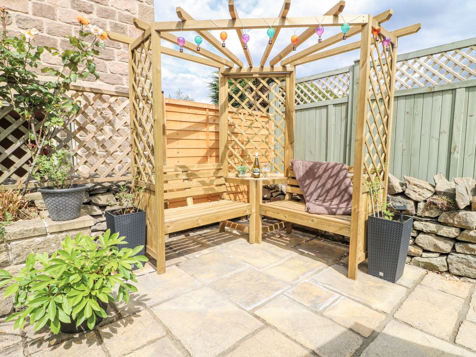 A garden seating area with a wooden pergola and benches at Clematis Cottage in Fritchley near Crich