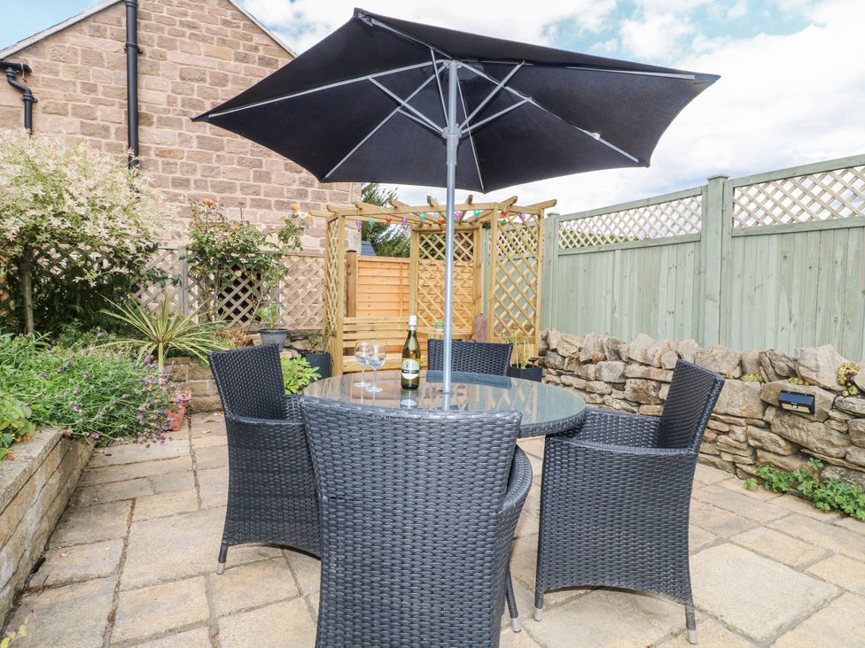 A garden with a table, chairs, and an umbrella at Clematis Cottage in Fritchley near Crich