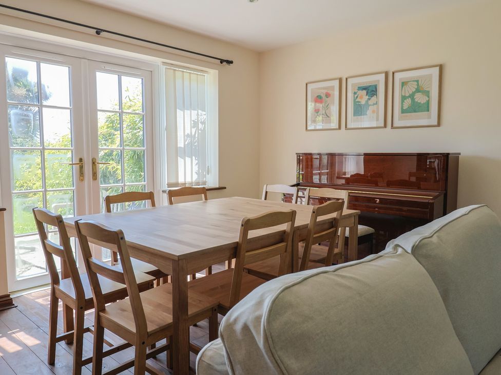 A dining room with a table and piano at 10 The Gardens Rousdon near Lyme Regis