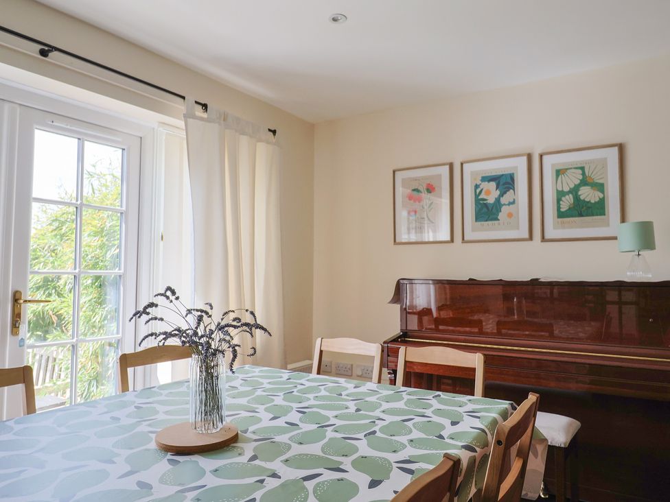 A dining room with a piano and table at 10 The Gardens Rousdon near Lyme Regis