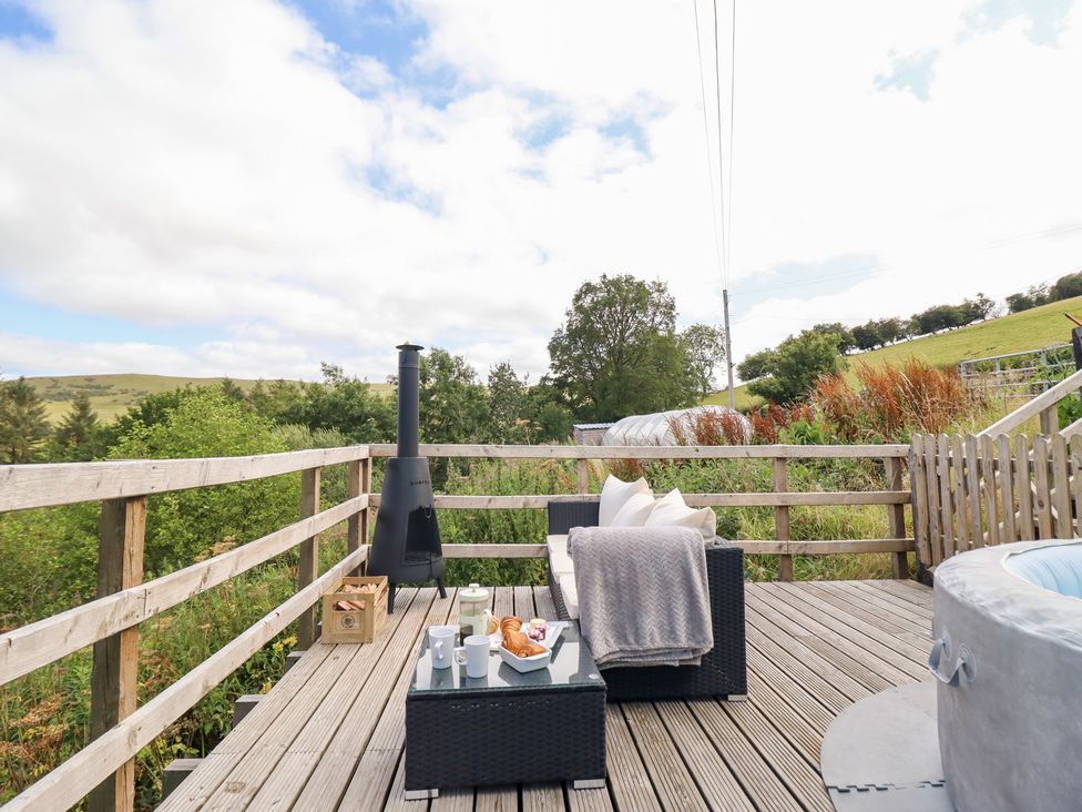 A deck with outdoor furniture and a hot tub at Cuckoo at Wild Valley Huts in Llanrhaeadr-Ym-Mochnant