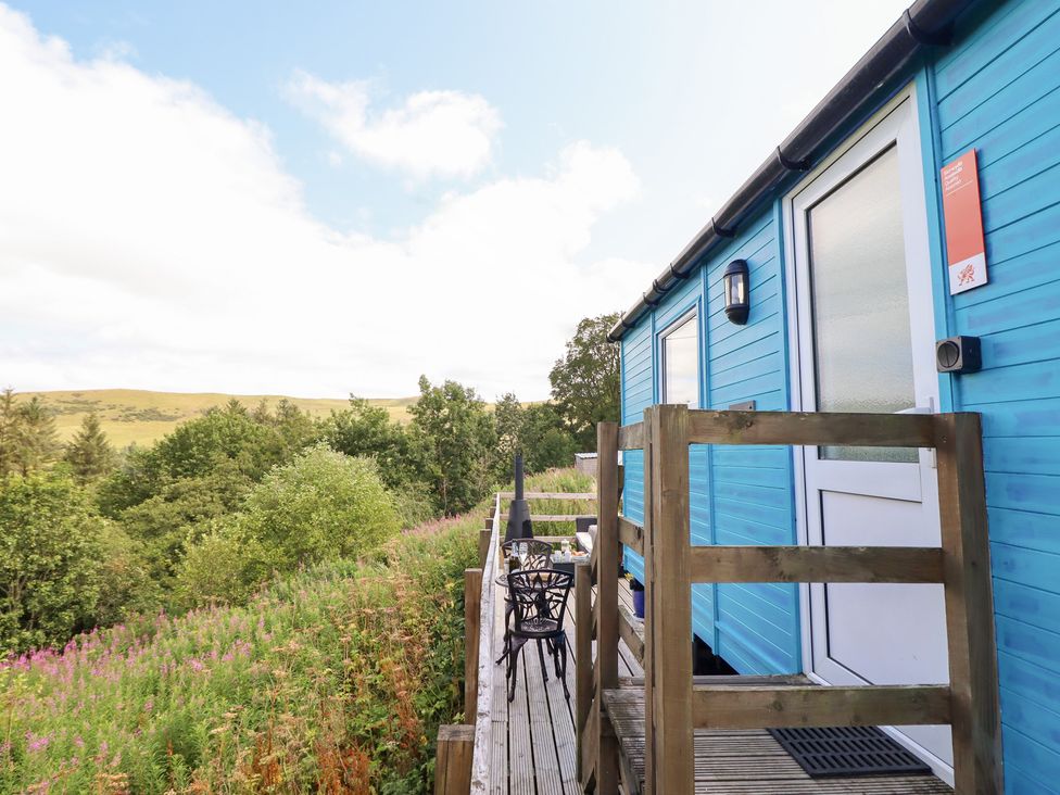 A blue hut with a deck and outdoor chair at Cuckoo at Wild Valley Huts Llanrhaeadr-Ym-Mochnant
