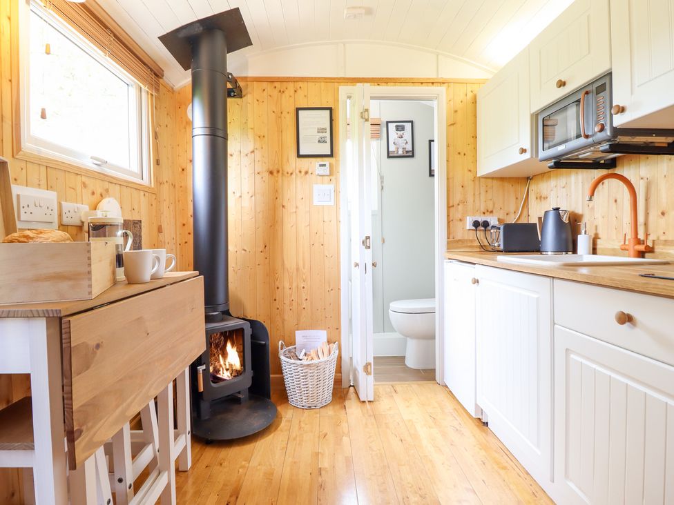A kitchen with a fireplace and wooden cabinets at Red Kite at Wild Valley Huts Llanrhaeadr-Ym-Mochnant