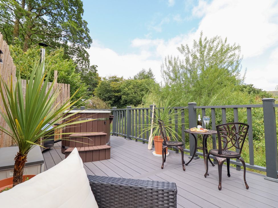 A deck with a hot tub, chairs, and a table at Red Kite at Wild Valley Huts Llanrhaeadr-Ym-Mochnant
