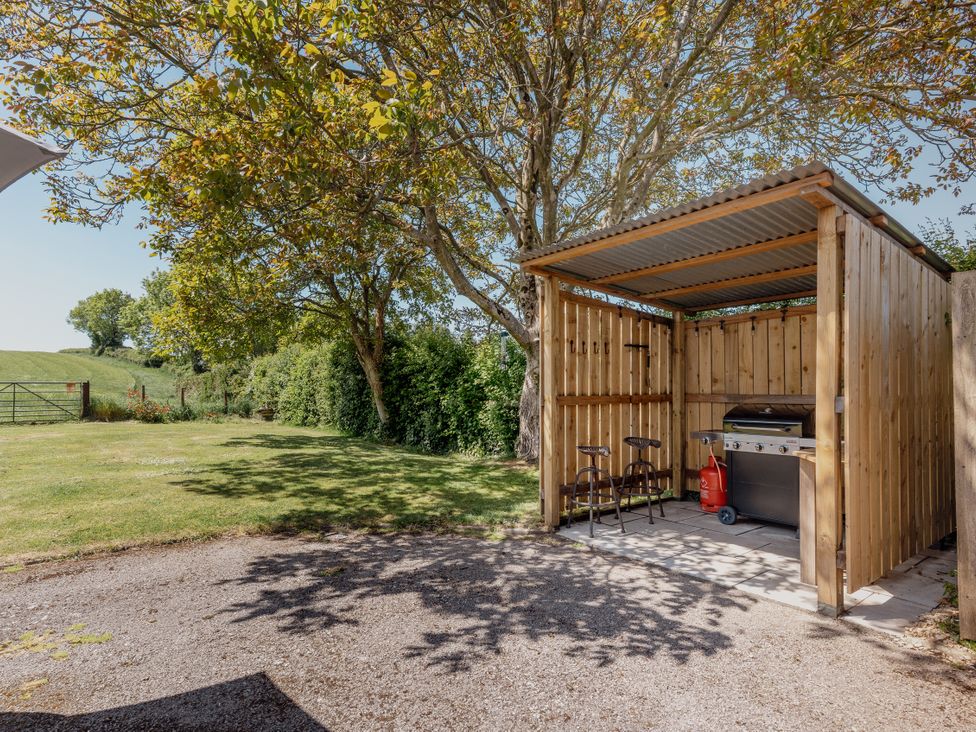 An outdoor grill and chairs in a shelter at Tokenhill Cottage in Piddletrenthide