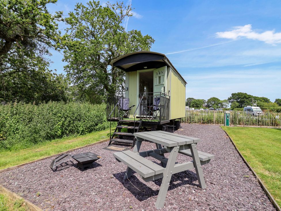 A shepherd's hut with a table and bench in front at Hop To It