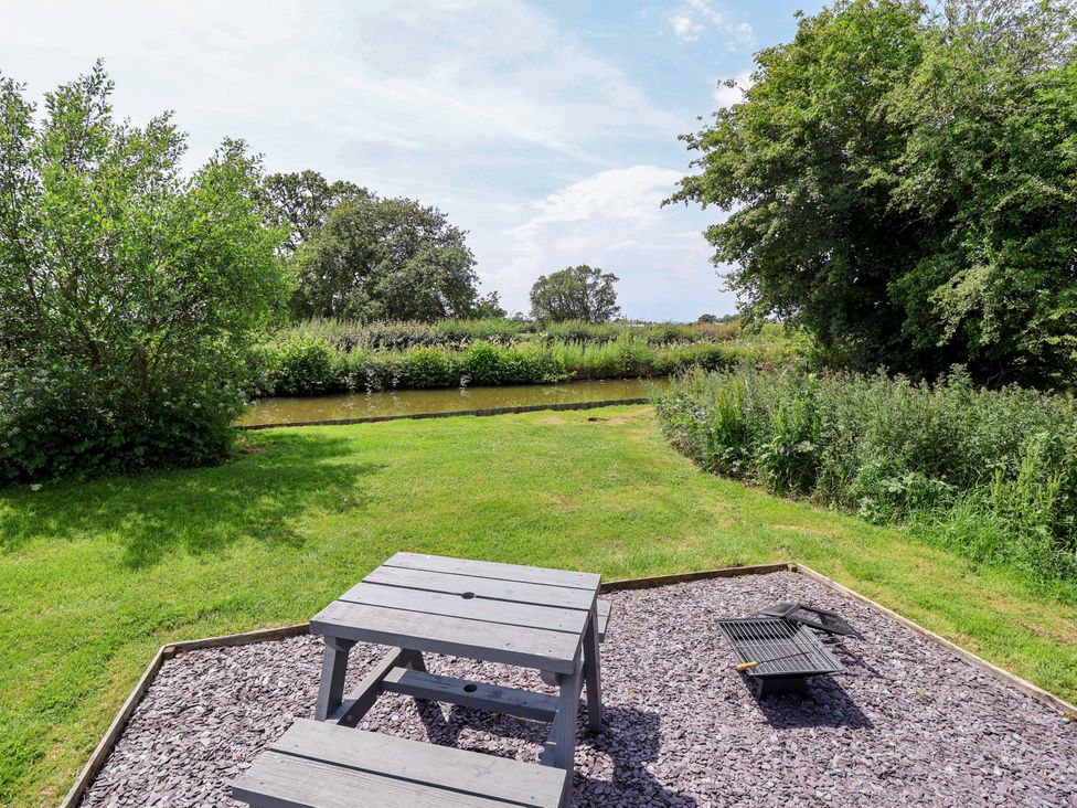 A garden with a table and grill overlooking a water area at Hop To It
