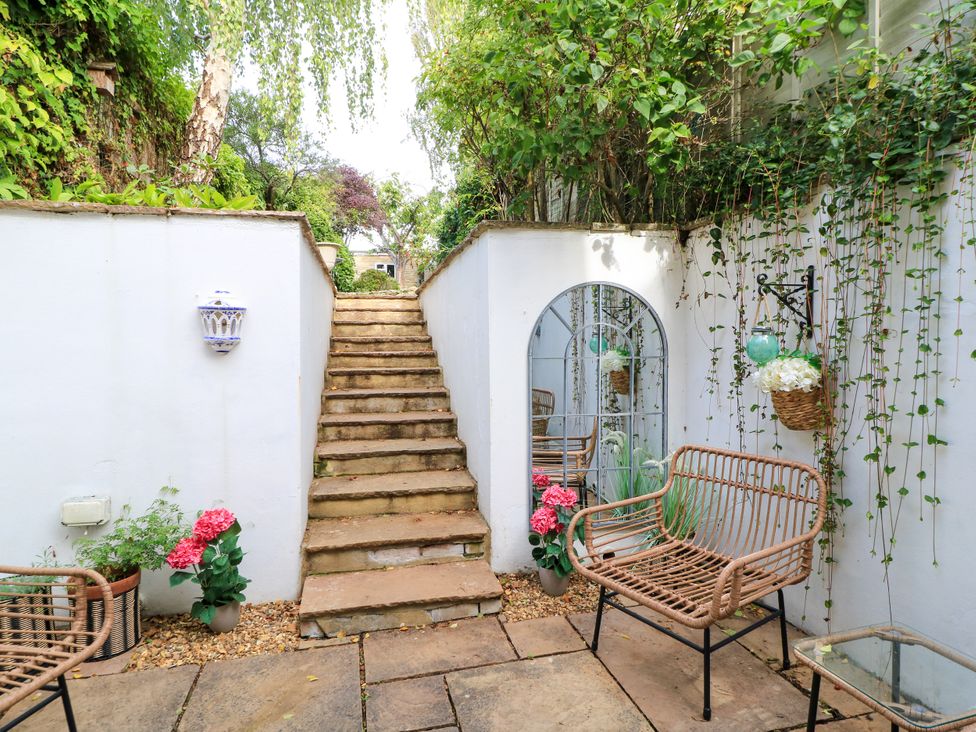 A garden with steps leading up and rattan chairs at Lower Pack Horse Cottage in Winchcombe