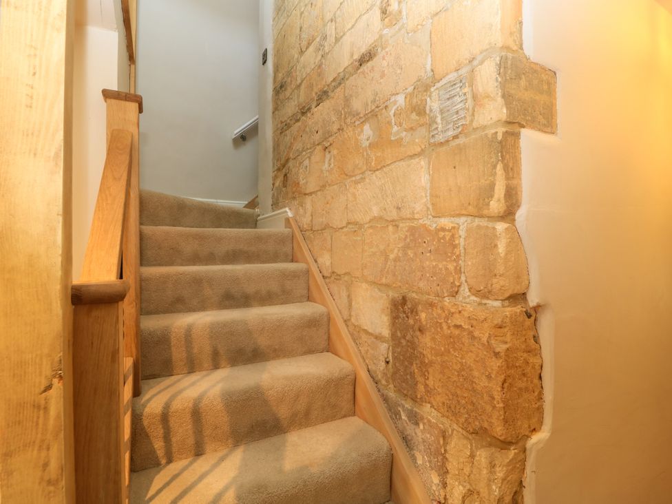 A staircase with carpet and a stone wall at Lower Pack Horse Cottage in Winchcombe