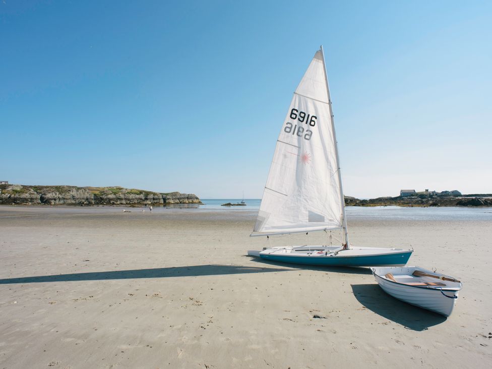 A sailboat and a small boat on a beach at Borth Arian Boat House in Rhoscolyn