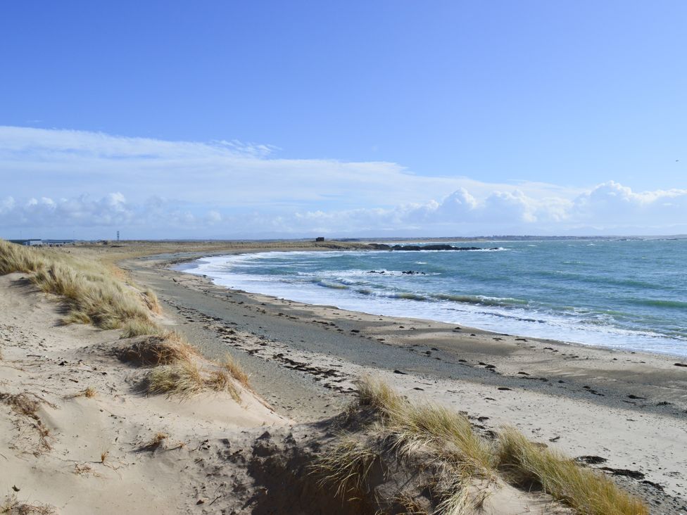 A beach with sand grass and waves at Borth Arian Boat House Rhoscolyn