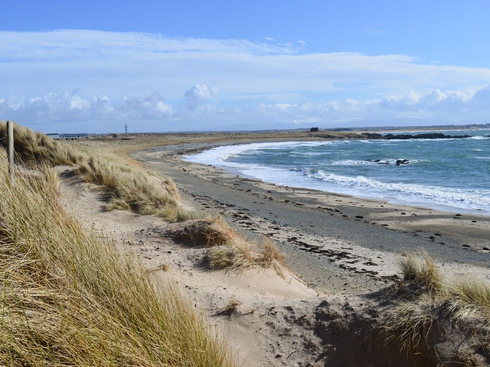 A beach with sand and grass along the shore at Borth Arian Boat House Rhoscolyn