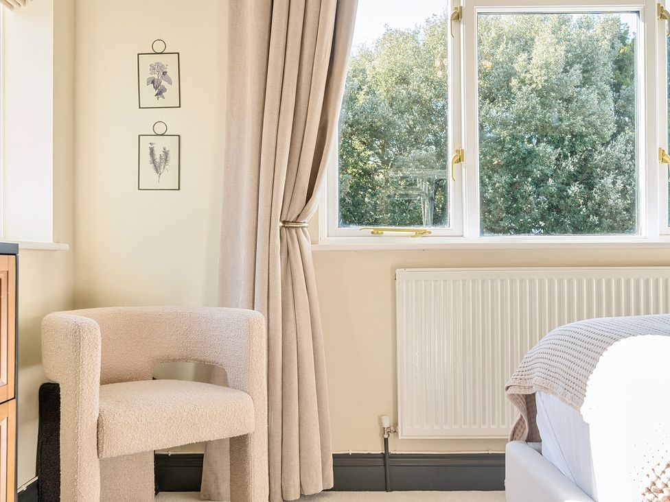 A bedroom with a chair, window, and curtains at 8 Newmarket Road Royston