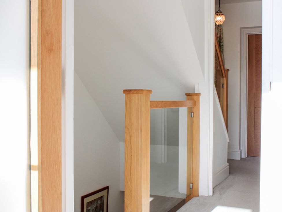 A staircase with a glass panel and wooden handrail at 2 Channel View Salcombe