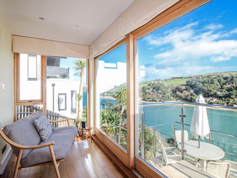A conservatory with a couch and a table overlooking a bay at 2 Channel View, Salcombe