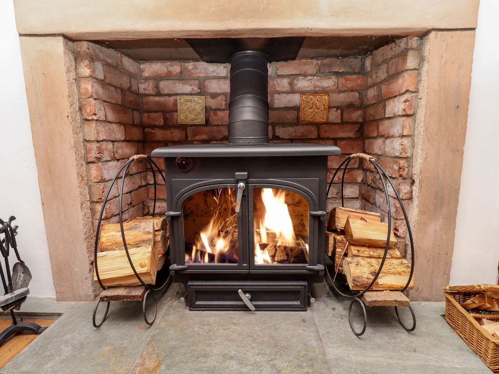 A lit wood burning stove with firewood on metal racks inside a brick fireplace at Seahares in Seahouses