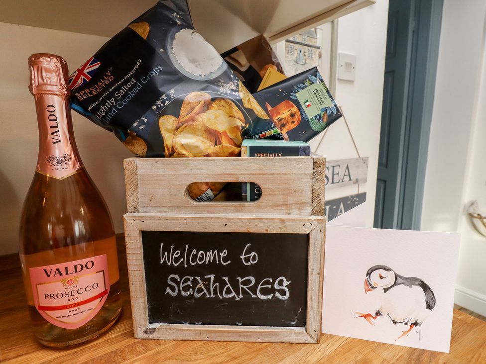 A wooden crate with snacks a bottle of Valdo prosecco and a card with a puffin illustration at Seahares in Seahouses