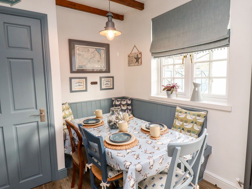 A dining area with a table set for four near a window with blue trim and wooden chairs at Seahares in Seahouses