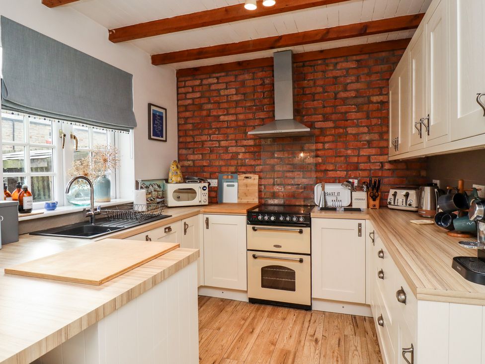 A kitchen with cream cabinets wooden countertops a stove with a chimney and a window with a grey blind at Seahares in Seahouses