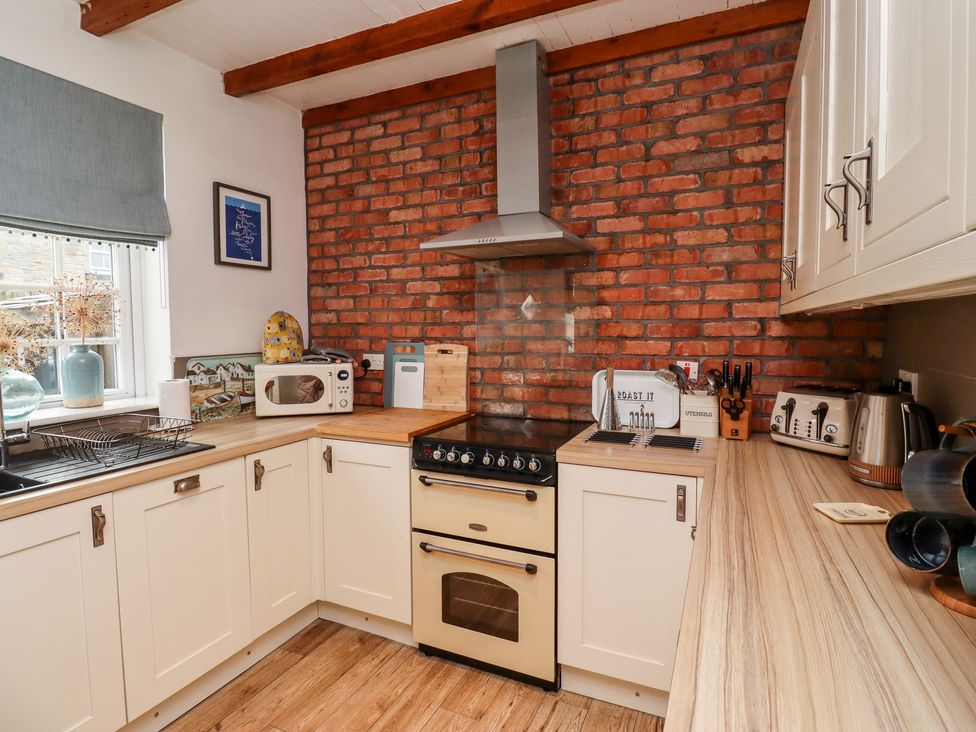 A kitchen with white cabinets wooden countertops a brick wall oven microwave toaster kettle and a window with a blind at Seahares in Seahouses