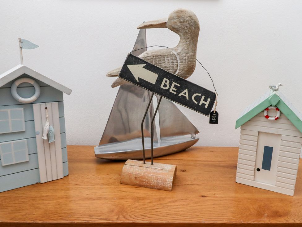 A wooden duck holding a beach sign with two small decorative beach huts and a metal sailboat on a wooden surface at Seahares in Seahouses