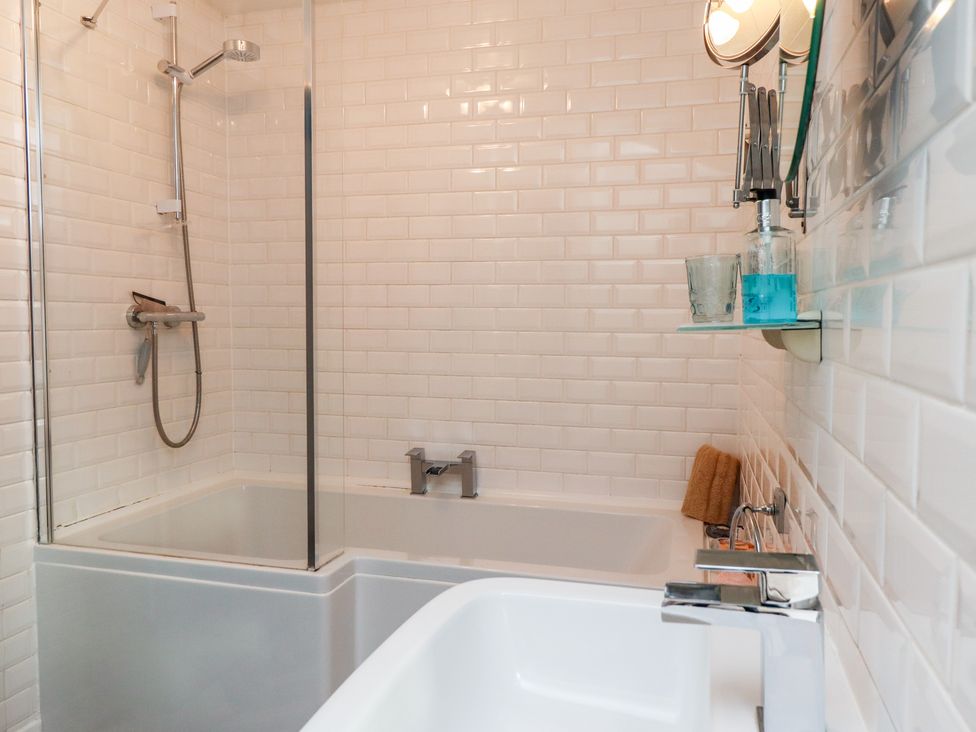 A bathroom with a bathtub shower combination white tiled walls and a sink with a faucet at Seahares in Seahouses