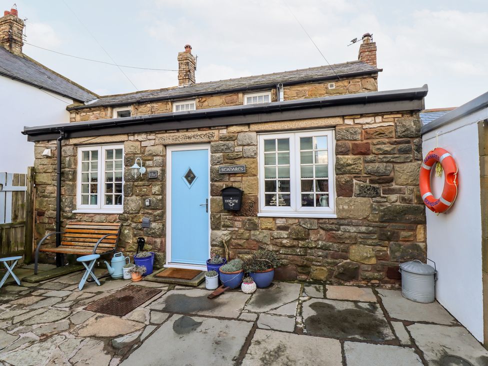 Stone house exterior with blue door bench potted plants and lifebuoy at Seahares in Seahouses