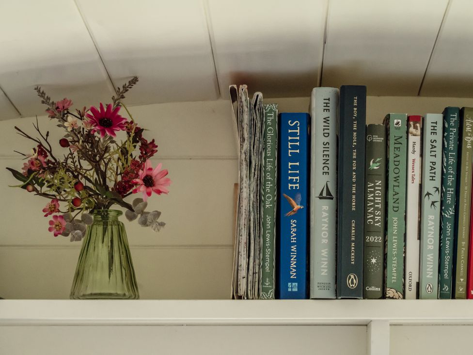 A shelf with flowers in a vase and various books at Hurdlemakers Hut Piddletrenthide