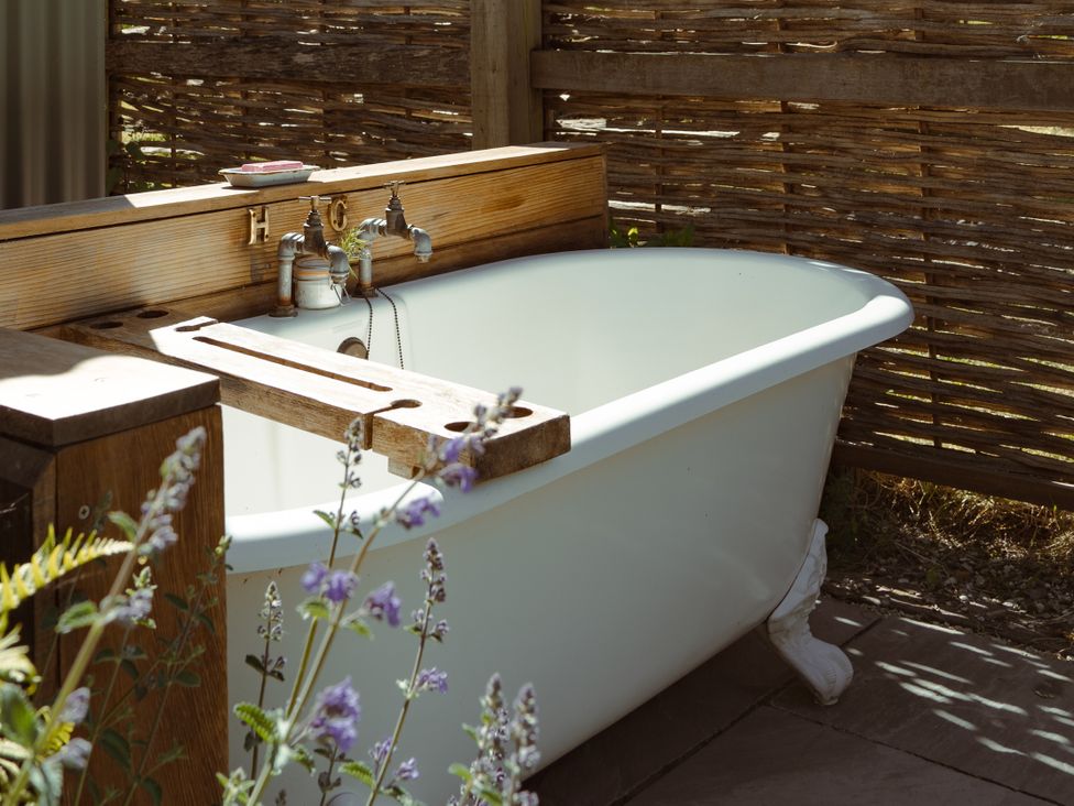 A bathtub with wooden features and plants at Hurdlemakers Hut in Piddletrenthide